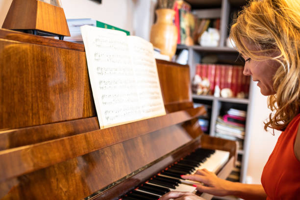 A pretty blonde is sitting at a piano at home playing a score